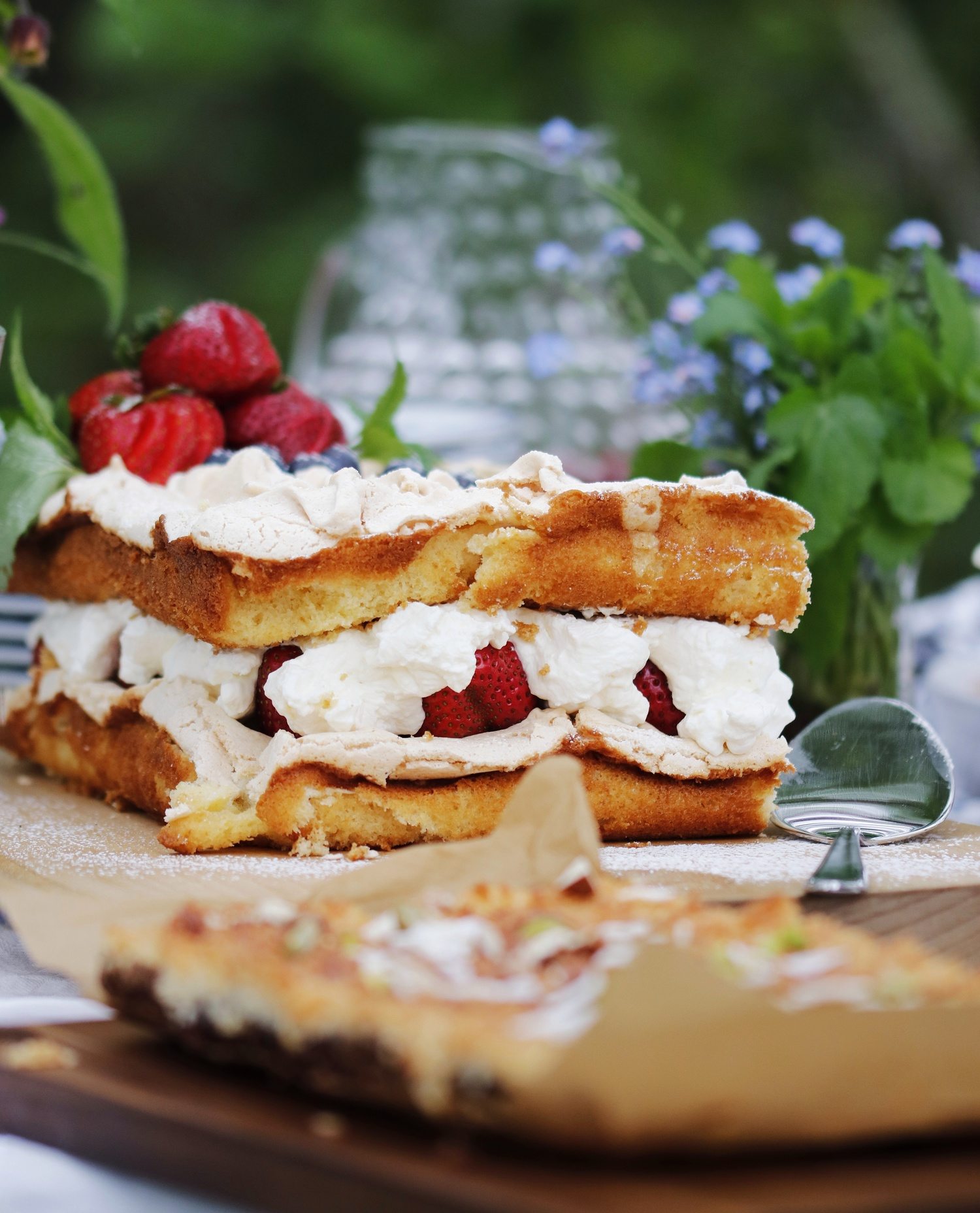 Sommartårta gjord i långpanna serverad med grädde och färska jordgubbar i lummig miljö