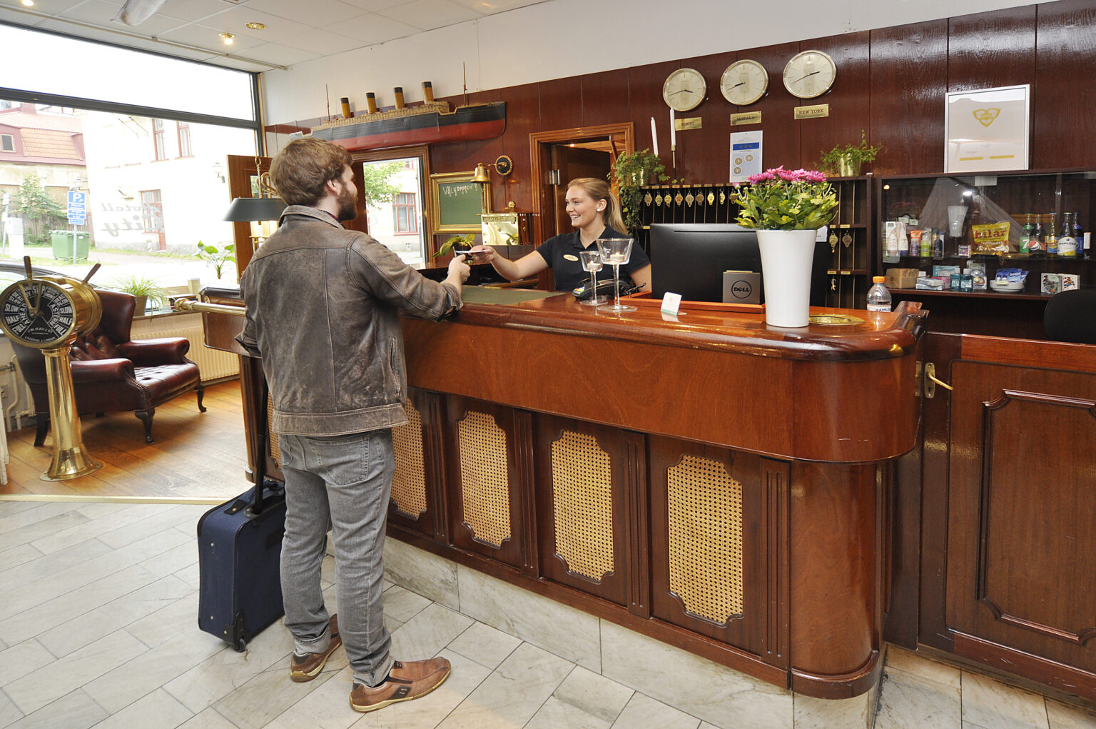 En gäst med resväska checkar in på hotell City i Motala, där receptionisten med ett leende lämnar ut nyckeln.