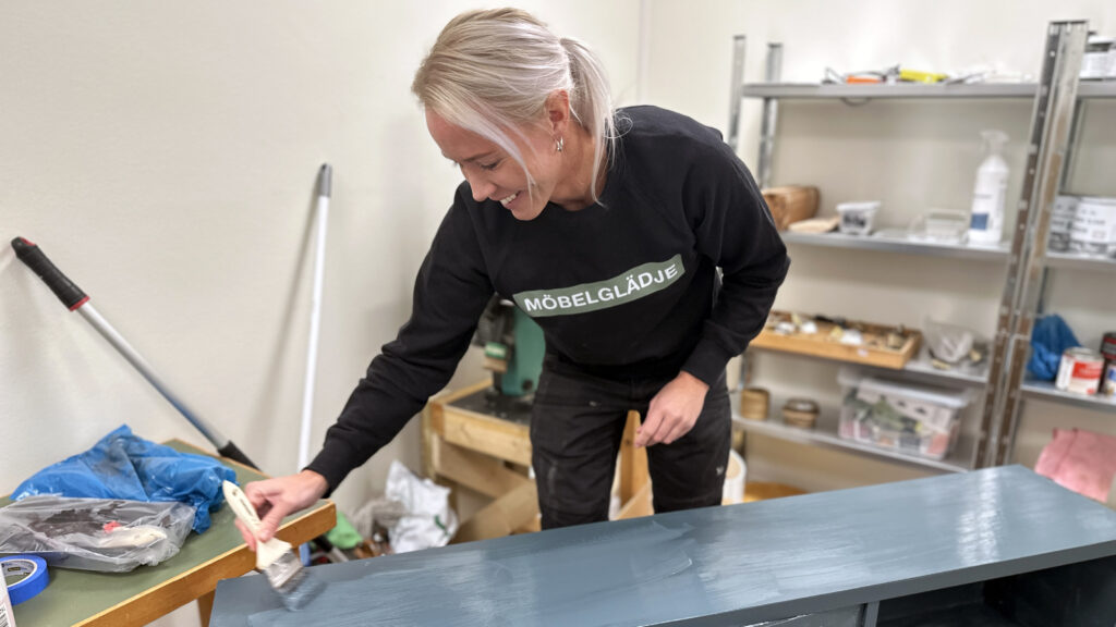 Josefin Arvidsson i butiken Möbelglädje målar en byrå i en blå färg inne i sin verkstad på Vadstenavägen.